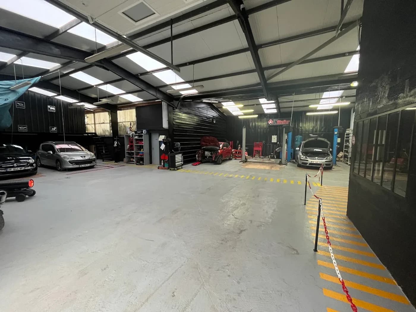 L'intérieur de l'atelier JH Auto : les ponts élévateurs, les postes de travail et les véhicules en cours d'intervention