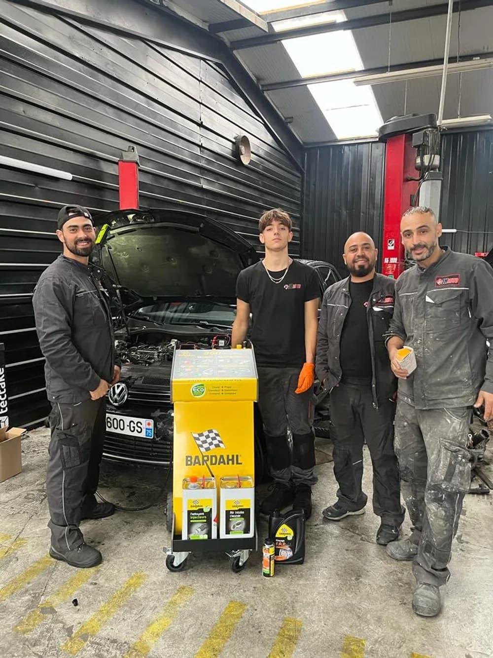 Quatre mécaniciens de l'équipe JH Auto devant une station de nettoyage moteur